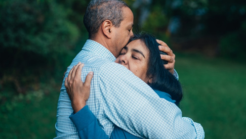 A man and woman embrace each other warmly in a lush green park
