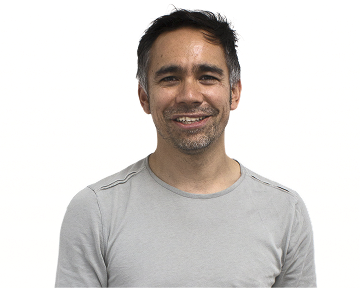 A man wearing a grey shirt smiles warmly at the camera