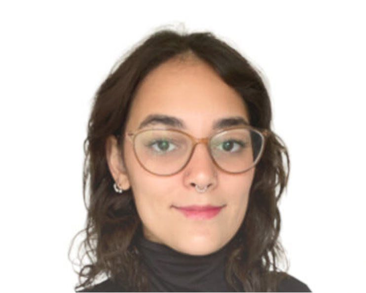A woman wearing glasses and a turtleneck sweater, smiling softly while looking towards the camera